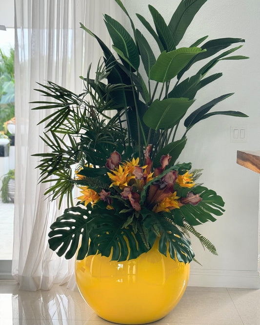 Plantes tropicales mélangées dans une jardinière globe jaune
